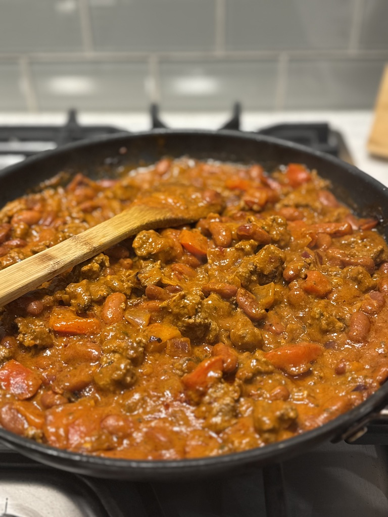 A skillet of Todd's favorite chili with a wooden spoon on the stovetop