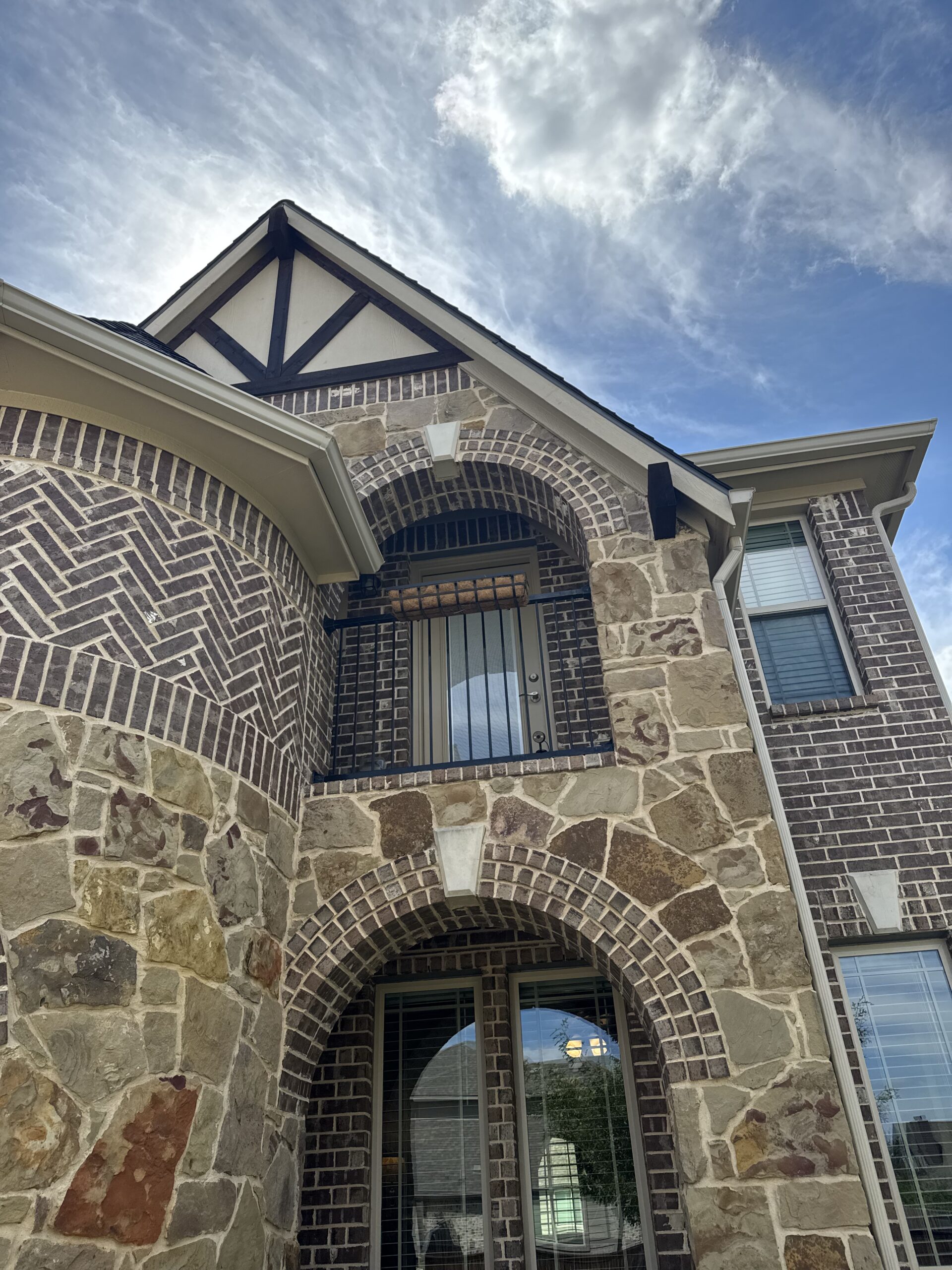 Jennifer Holland's North Texas home with its finished new roof, stone and brick facade under a blue sky